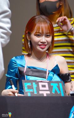 a woman with red hair holding a sign and wearing a face mask while standing next to other people