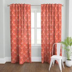 a white chair sitting in front of a window next to a curtain with an orange flower pattern