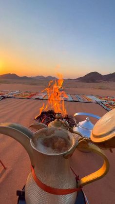 a tea pot sitting on top of a stove next to a campfire in the desert