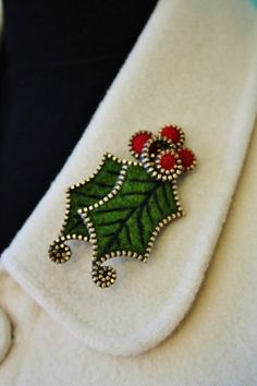 a close up view of a christmas brooch on a white jacket with holly leaves