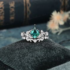 a ring with an emerald colored stone surrounded by leaves on top of a black cloth