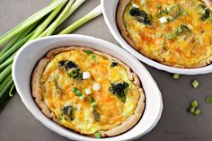 two white bowls filled with quiche on top of a table next to asparagus