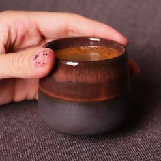 a hand holding a small brown cup with pink dots on its thumb and fingernails