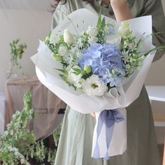 a woman holding a bouquet of blue and white flowers on her left hand while talking on the phone