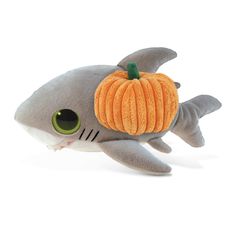 a stuffed shark with an orange pumpkin on it's head and green eyes is laying down