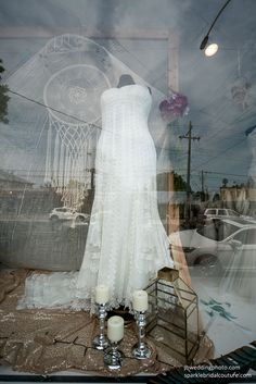 a wedding dress and candles are on display in a shop window with an image of a dream catcher behind it