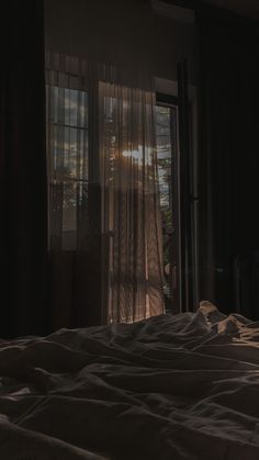 an unmade bed in front of a window with sheer curtains and the sun shining through