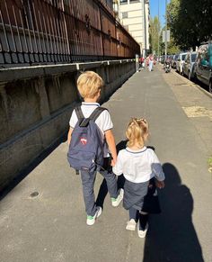 two little kids walking down the street with backpacks on their back and one holding hands