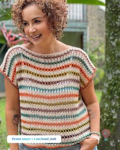 a woman with curly hair wearing a multicolored crochet top and jeans