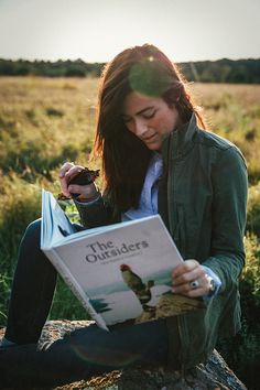 a woman sitting on a rock reading a book