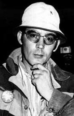 a man wearing a hat and glasses sitting at a table with a drink in front of him