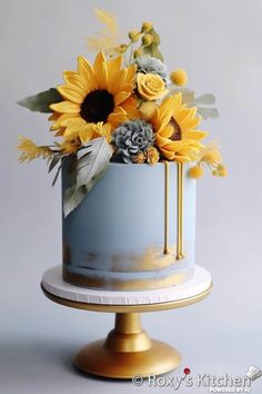 a blue and gold cake with sunflowers on top is sitting on a stand