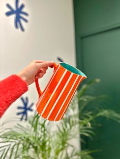 a person holding an orange and white striped coffee mug in front of a potted plant