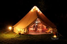 a tent is lit up at night in the grass with lights on it and there are two people sitting outside