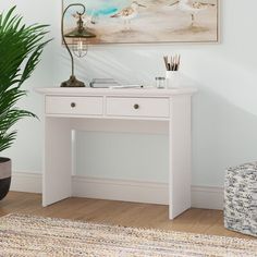 a white desk with a plant in front of it and a painting on the wall