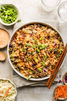 a bowl filled with rice and vegetables next to chopsticks on a napkin near other bowls