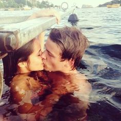 a man and woman are kissing in the water near a buoy on a boat