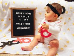 a baby sitting on a bed with scissors and a sign that says sorry boys daddy is my valentine