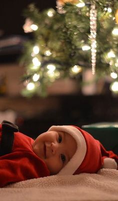 a baby wearing a santa hat laying on top of a blanket next to a christmas tree