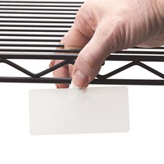 a hand holding a white card over a metal bed frame with slats on it