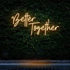 a neon sign that says better together in front of a wall covered with green leaves