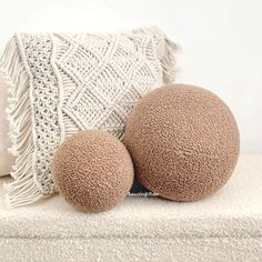 two round pillows sitting next to each other on a white surface with a crocheted pillow behind them