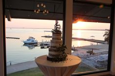 a wedding cake sitting on top of a table next to a large window overlooking the water