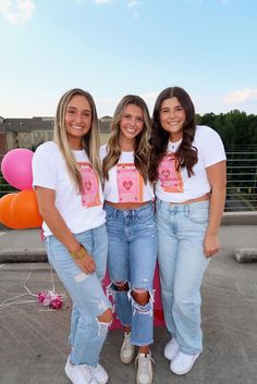 three girls standing next to each other in jeans and t - shirts with hearts on them