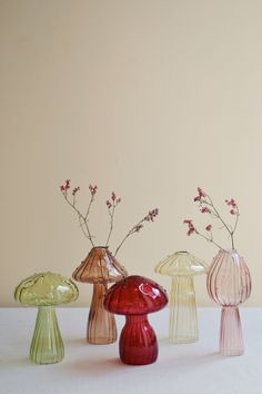 four glass vases with flowers in them on a white tableclothed surface next to a beige wall