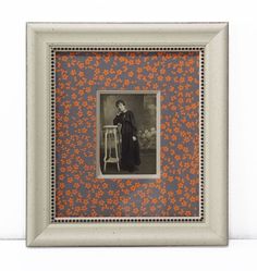 an old photo with orange flowers on it in a white frame, hanging on the wall