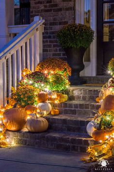 pumpkins and gourds are lit up on the steps in front of a house