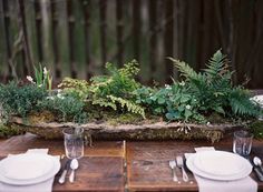 the table is set with white plates and silverware on it, along with greenery