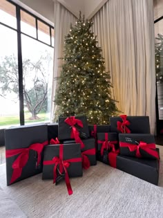 a group of black boxes with red bows on them sitting in front of a christmas tree