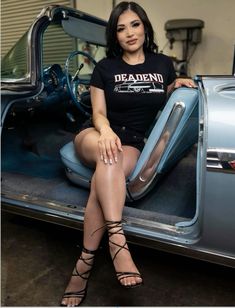 a woman sitting on the back of a car with her legs crossed and wearing gladia sandals