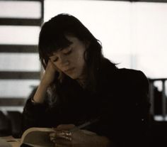 a woman sitting at a table writing on a book and holding a pen in her hand