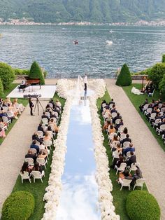 an outdoor wedding ceremony is set up on the lawn by the water and surrounded by greenery