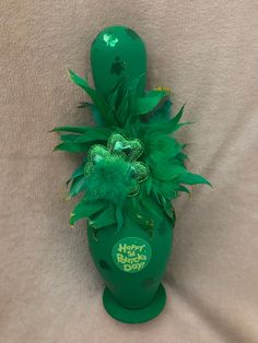 a green vase filled with lots of green flowers on top of a white sheet covered floor