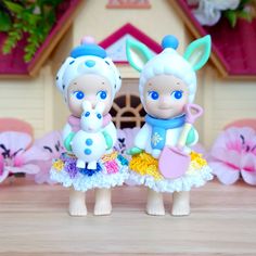 two little figurines standing next to each other in front of a doll house