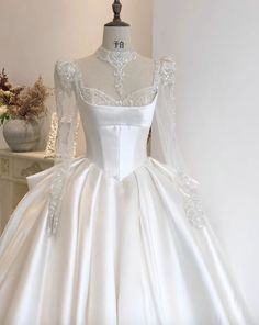 a white wedding dress on a mannequin in front of a vase with flowers