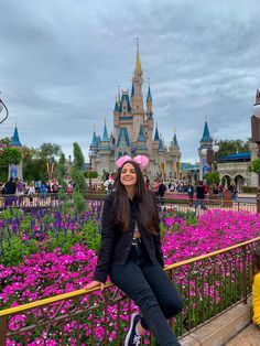 a woman sitting on a rail in front of a castle with purple flowers around her