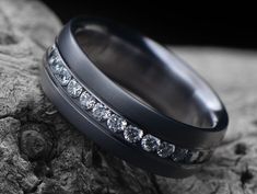 a black wedding band with channeled diamonds on it sitting on top of a rock