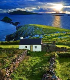 a small white house sitting on top of a lush green hillside next to the ocean