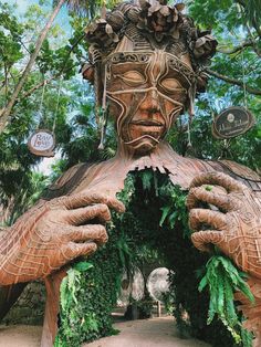 a large wooden statue with plants growing out of it's face and hands over his eyes