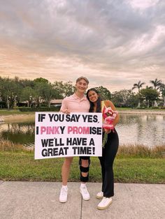 two women standing next to each other holding a sign that says if you say yes, i pinky promise we'll have a great time