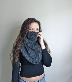 a woman with long hair wearing a knitted scarf over her face and looking at the camera