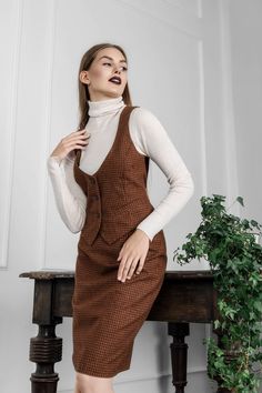 This brown checkered wool suit is handmade by Tauri Look designers from the highest quality Italian wool. A semi-formal women's Suit with a waistcoat gives freedom to move, while the lace in the back allows you to adjust the tightness of the vest. Together with a pencil shape skirt, it allows you to create an image of an attractive business woman. This classic women's suit with a vest is ideal for you if, when the weather gets cold, you instantly start looking for clothes that are not only stylish but also guarantee warmth and coziness.  When you wear this formal women's suit, you will perfectly fit the norms of business etiquette. You can easily match the skirt with another black, grey, or even solid green blazer, too. The waistcoat looks great not only with dark color skirts but also whe Fall Tweed Dress With Buttons And Fitted Style, Fitted Tweed Dress With Buttons For Fall, Fitted Plaid Vest For Winter, Winter Brown Fitted Skirt Suit, Brown Fitted Skirt Suit For Winter, Fitted Skirt Suit With Pockets For Fall, Fitted Tweed Dress With Buttons For Work, Fitted Sleeveless Tweed Dress For Winter, Fitted Houndstooth Tweed Dress For Office