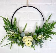 a wreath with white flowers and greenery hanging on a brick wall in the shape of a circle