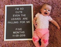 a baby laying next to a sign that says i'm so cute even the leaves are falling for me