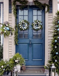 a blue front door decorated with christmas wreaths and greenery