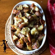 a white bowl filled with potatoes sitting on top of a wooden table next to a red and white checkered napkin